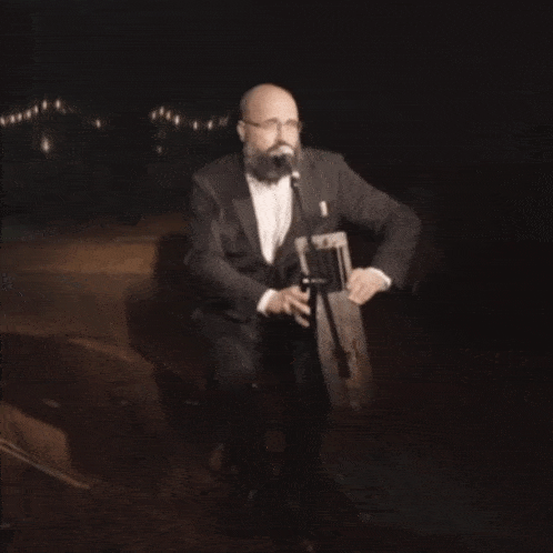 a man in a tuxedo and bow tie sings into a microphone