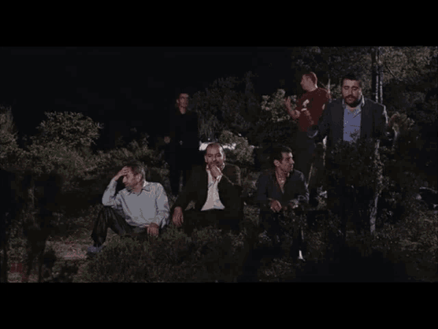 a group of men are sitting in a dark forest with their arms in the air