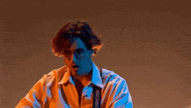 a man wearing glasses and suspenders is standing in a dark room .