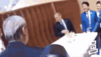 a blurry picture of a man sitting at a table with other men .