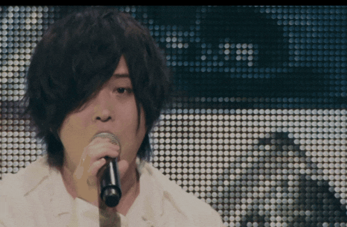a man is singing into a microphone in front of a screen with dots