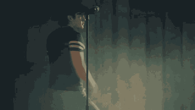 a man singing into a microphone in a dark room with smoke behind him