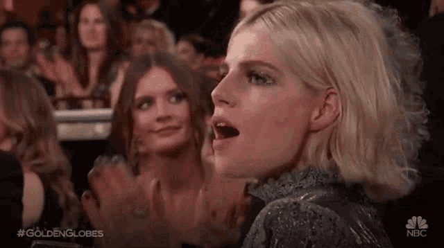 a woman is sitting in a crowd of people with her mouth open and a surprised look on her face .