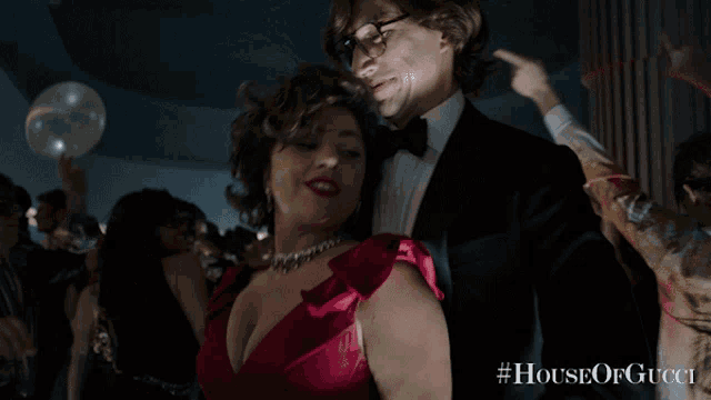 a woman in a red dress is dancing with a man in a tuxedo with #houseofgucci on the bottom