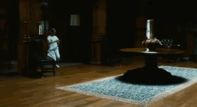 a woman in a white dress is standing in a dark room with a table