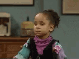 a little girl is making a funny face while sitting at a table in a living room .