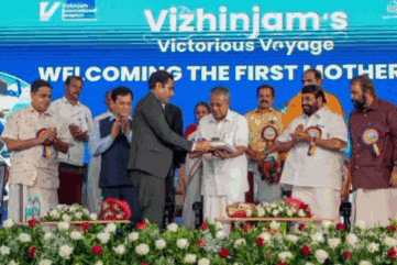 a group of men are standing in front of a blue sign that says vizhinjam 's victorious voyage