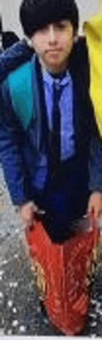 a young boy in a blue shirt and tie is standing next to a red bucket .