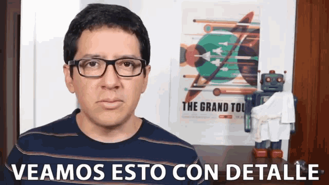 a man wearing glasses stands in front of a poster for the grand tour