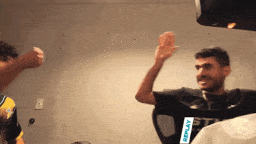 a man wearing a black shirt that says replay is giving another man a high five
