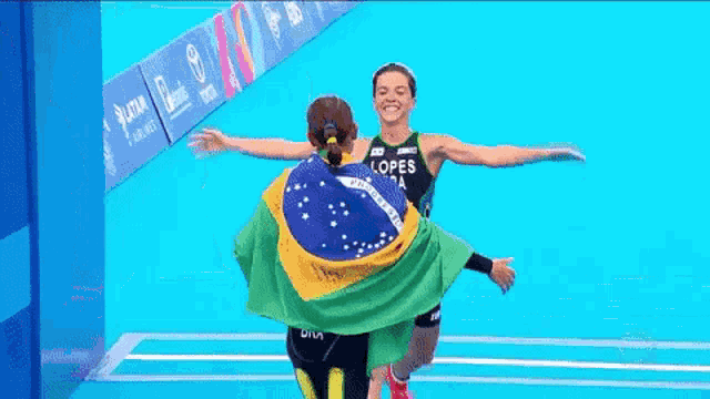 two female athletes are hugging each other while holding a brazilian flag .