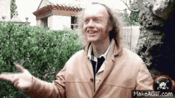 a man in a brown jacket is pointing at something while smiling .