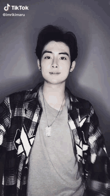 a young man wearing a plaid shirt and a necklace has a tiktok watermark on his photo