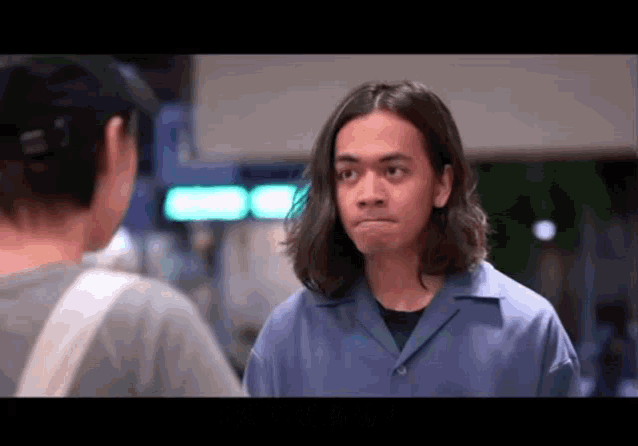 a man with long hair is standing next to a woman and making a funny face .