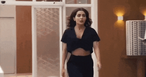 a woman in a crop top and pants is walking through a doorway .