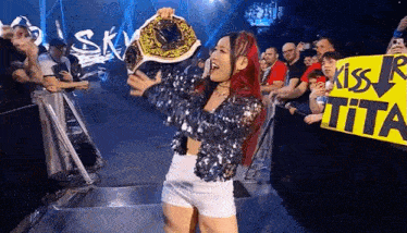 a woman is holding a championship belt in front of a crowd of people .