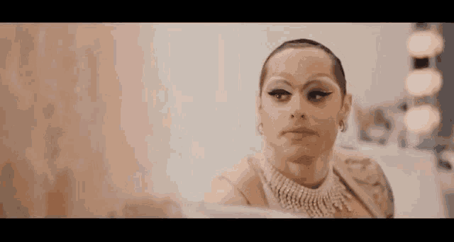 a drag queen is looking at herself in a mirror while wearing a pearl necklace .