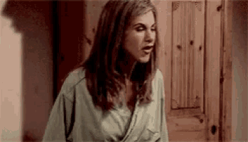 a woman in a robe is standing in front of a wooden door and looking at the camera .