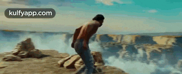 a man without a shirt is jumping off a cliff into the water .