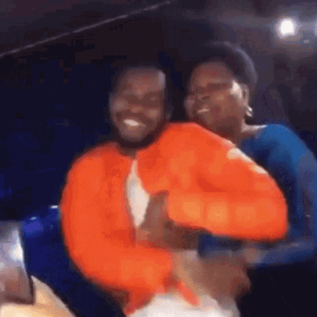a man in an orange jacket is holding a woman in a blue shirt .