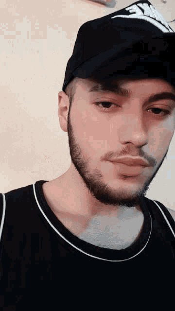 a man with a beard wearing a black nike hat and a black tank top