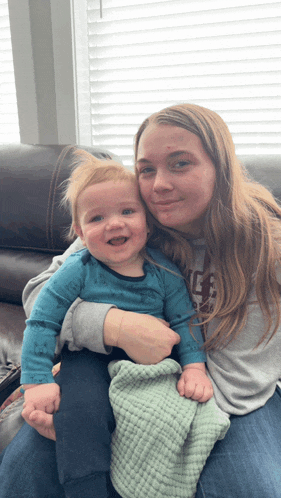 a woman is holding a baby who is wearing a blue shirt with the letter g on the front
