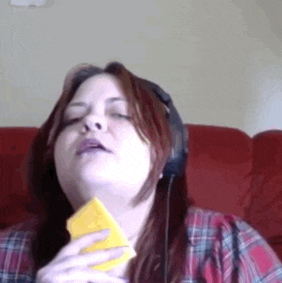 a woman wearing headphones holds a piece of cheese in her hand