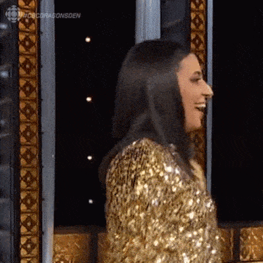 a woman wearing a gold sequined jacket is standing in front of a window .