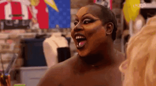 a drag queen with a shaved head is making a funny face with her mouth open .
