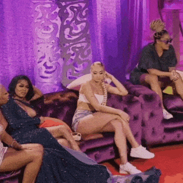 a group of women are sitting on purple couches in front of a purple curtain .