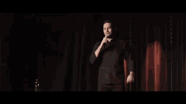 a man in a black shirt is holding a microphone on a stage