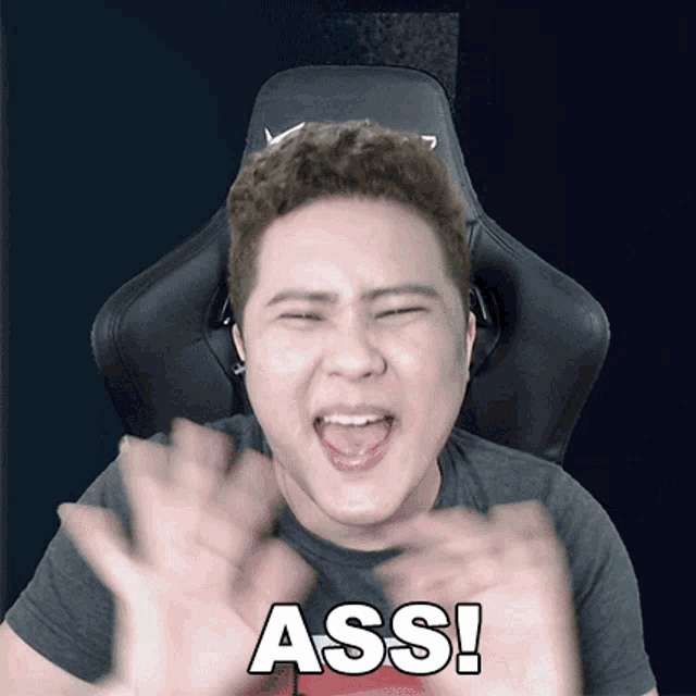 a man sitting in a chair with his mouth open and the word ass written on his shirt