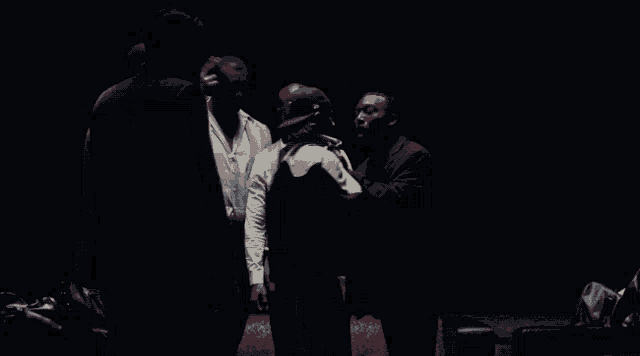 a group of men standing in a dark room with one wearing a hat