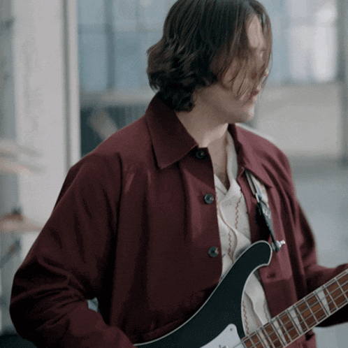 a man in a maroon jacket plays a guitar