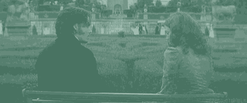 a man and a woman are sitting on a bench holding hands in a park .