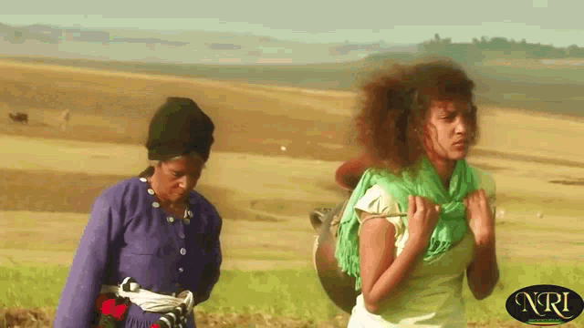 two women walking in a field with nri on the bottom