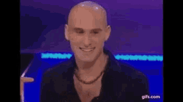 a bald man is smiling and clapping his hands while sitting in front of a blue background .