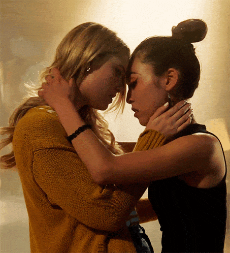 a woman in a yellow sweater is kissing another woman in a black tank top