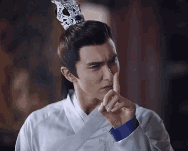 a man with a crown on his head has his finger on his nose