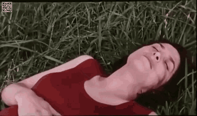 a woman in a red dress is laying on her stomach in the grass with her eyes closed .