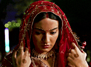a woman wearing a red and gold veil looks down
