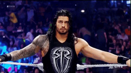 roman reigns is standing in the ring with his arms outstretched .