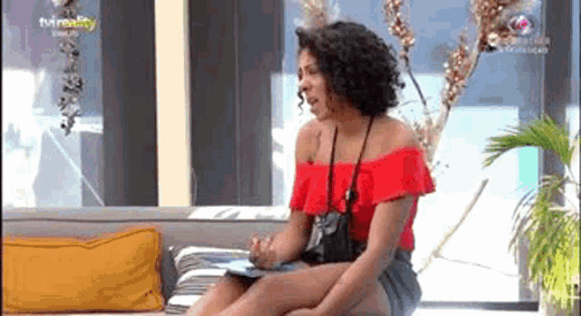 a woman in a red top is sitting on a couch .