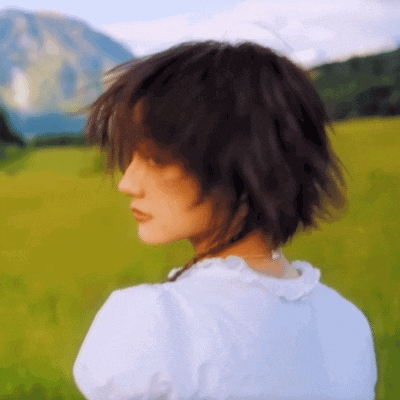 a woman in a white shirt is standing in a field with mountains in the background