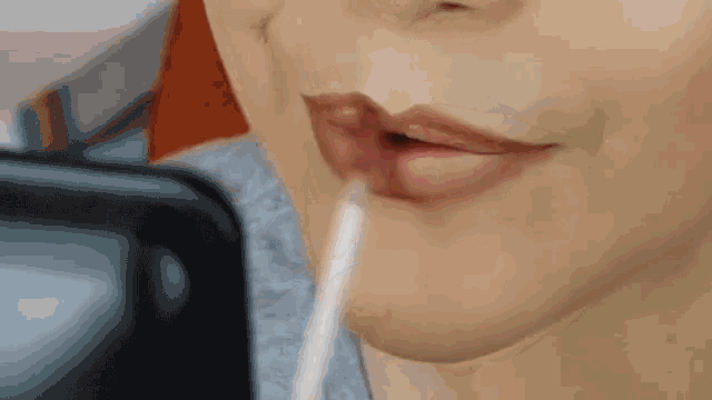 a woman is applying lip gloss with a straw in her mouth .