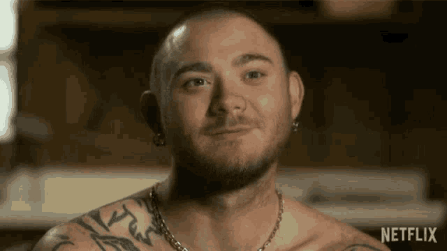 a shirtless man with tattoos on his chest is smiling in a netflix video