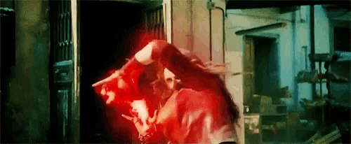 a woman in a red jacket is standing in a dark room with red light coming out of her eyes .