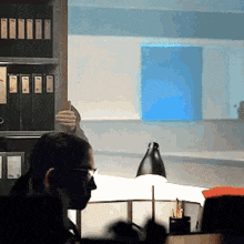 a man wearing glasses sits at a desk in front of a large window