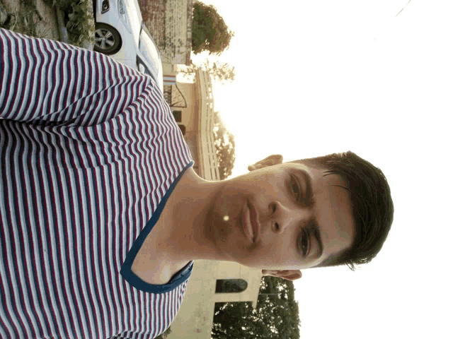 a young man in a striped shirt stands in front of a car