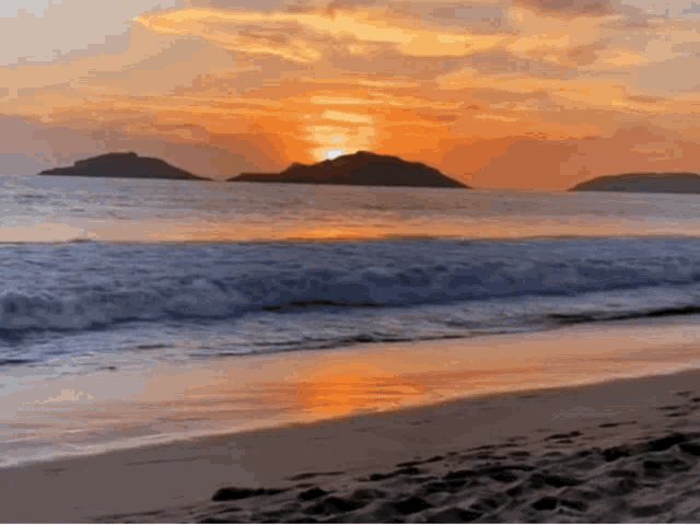 a sunset over a beach with a few islands in the distance